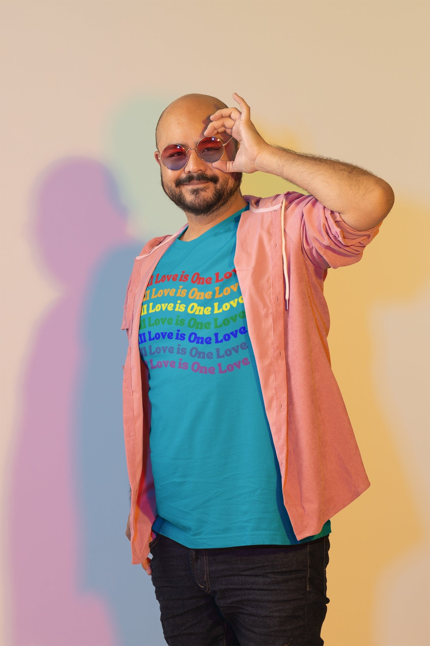smiling bald headed bearded man wearing an aqua "all love is one love" graphic (repeated in rainbow colors) t-shirt under an open pink shirt