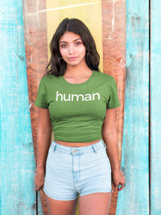 beautiful hispanic young woman standing in front of a worn yellow and red surf board leaning on a faded blue fence wearing a green t-shirt with "human" graphic