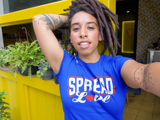 woman with dreadlocs wearing royal blue t-shirt with "spread love" graphic with red heart replacing the "o" while outside restaurant