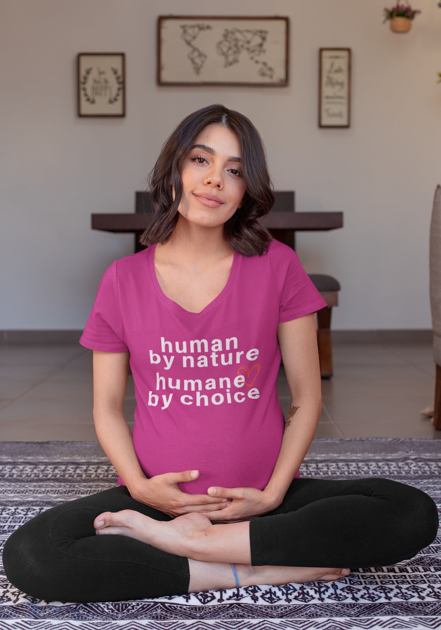 beautiful pregnant woman in yoga crossed legs on mat wearing a berry t-shirt with "human by nature, humane by choice" graphic.