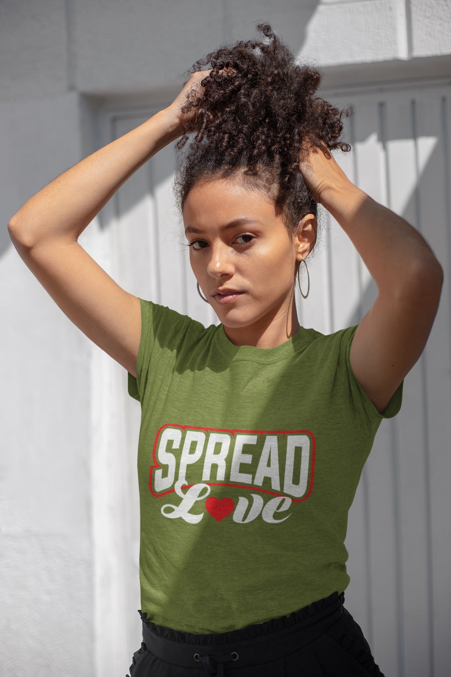 beautiful woman playing with her curly hair wearing an olive green t-shirt with "spread love" graphic with red heart replacing the "o" 