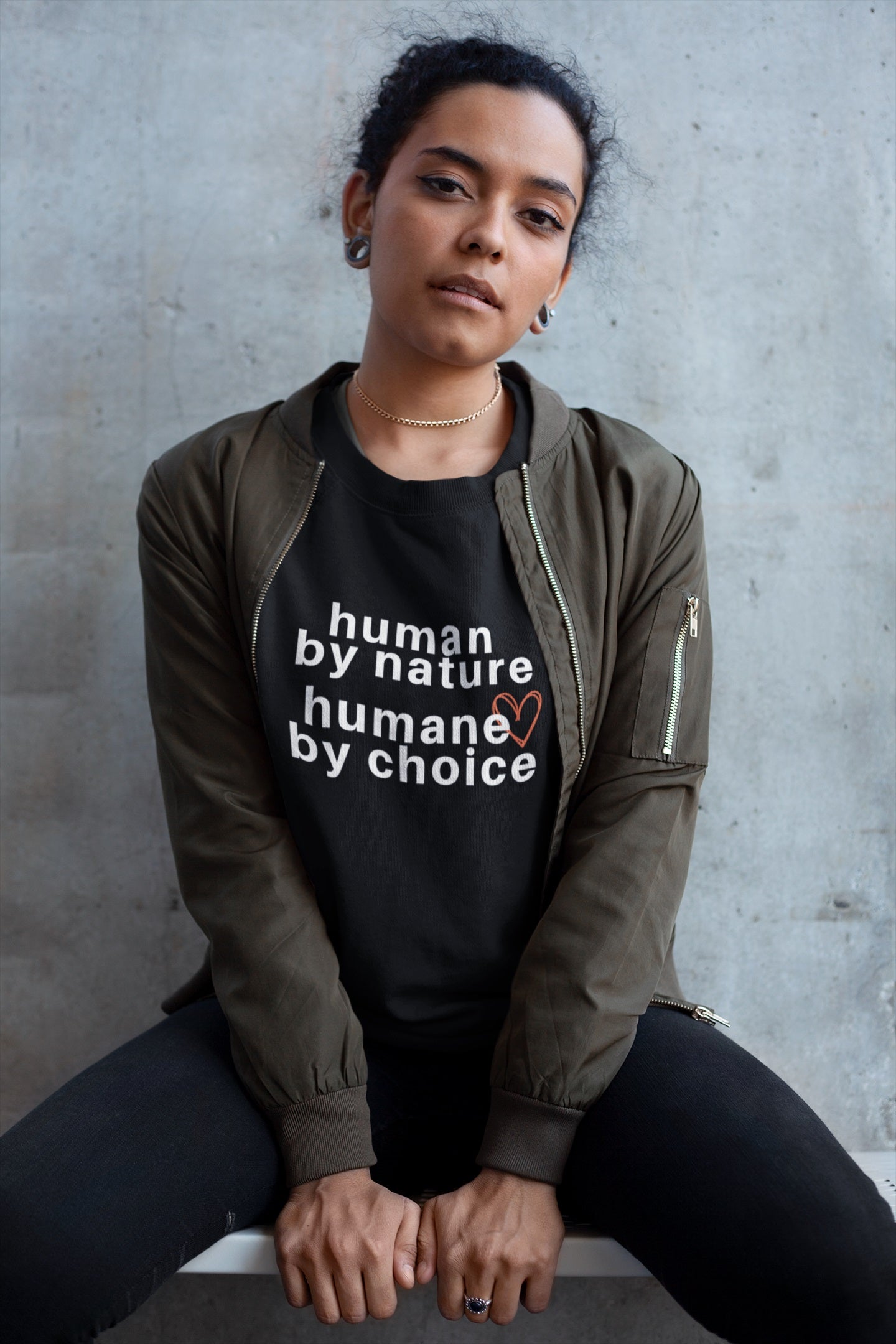 woman sitting on stool wearing black nelalena humane by choice sweatshirt under green jacket