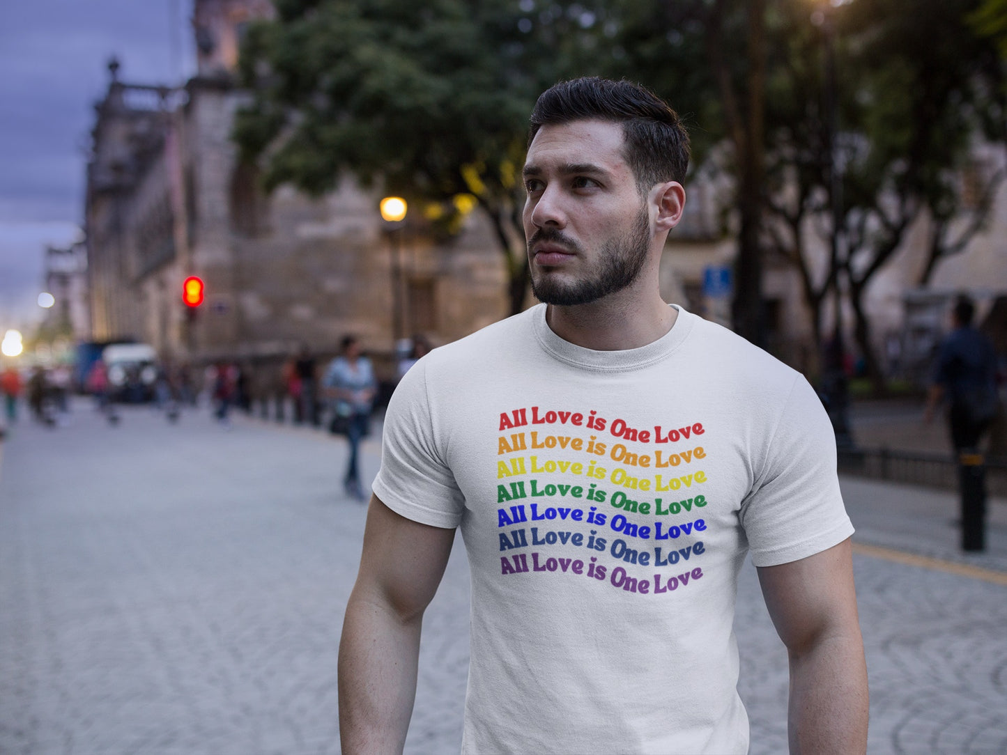 muscular man walking on the street in early evening wearing white "all love is one love" graphic (repeated in rainbow colors) t-ahirt