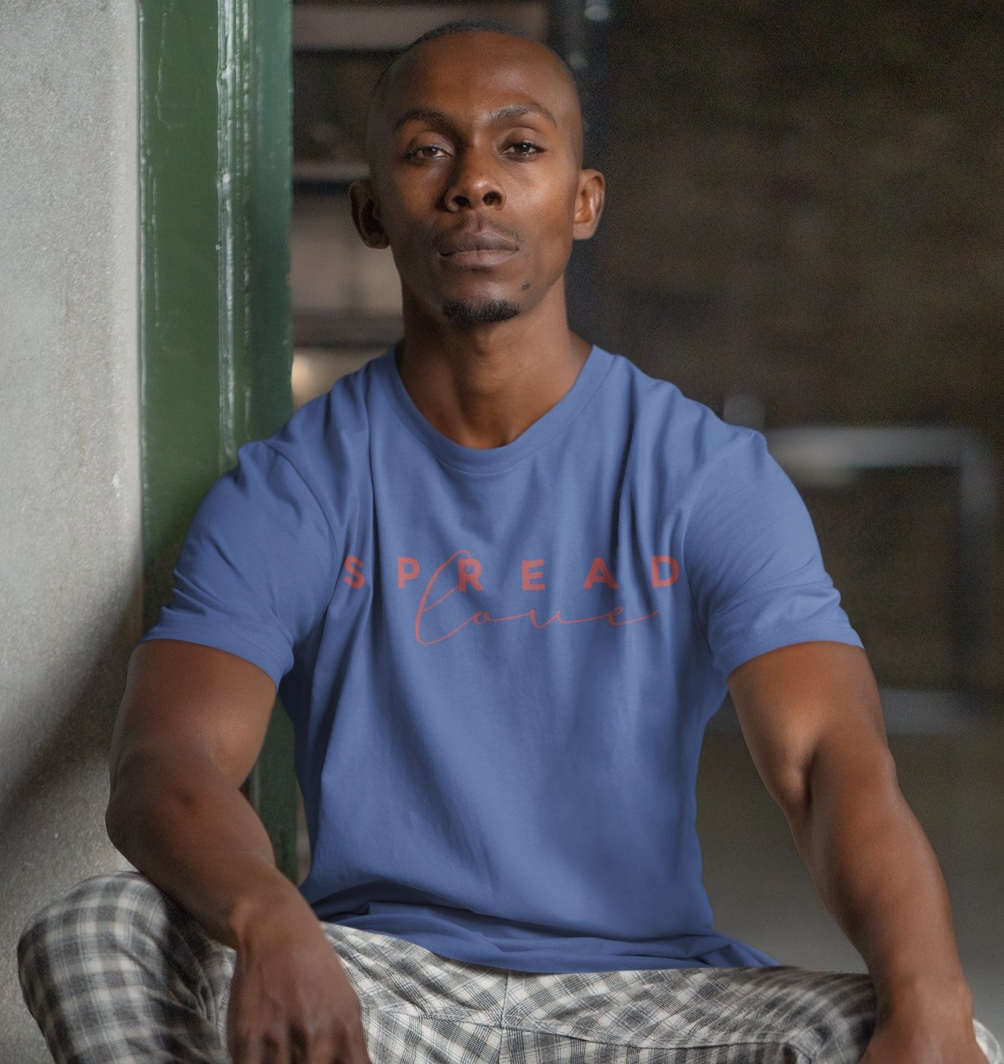 man sitting on a step against a green wall wearing a blue spread love t-shirt 