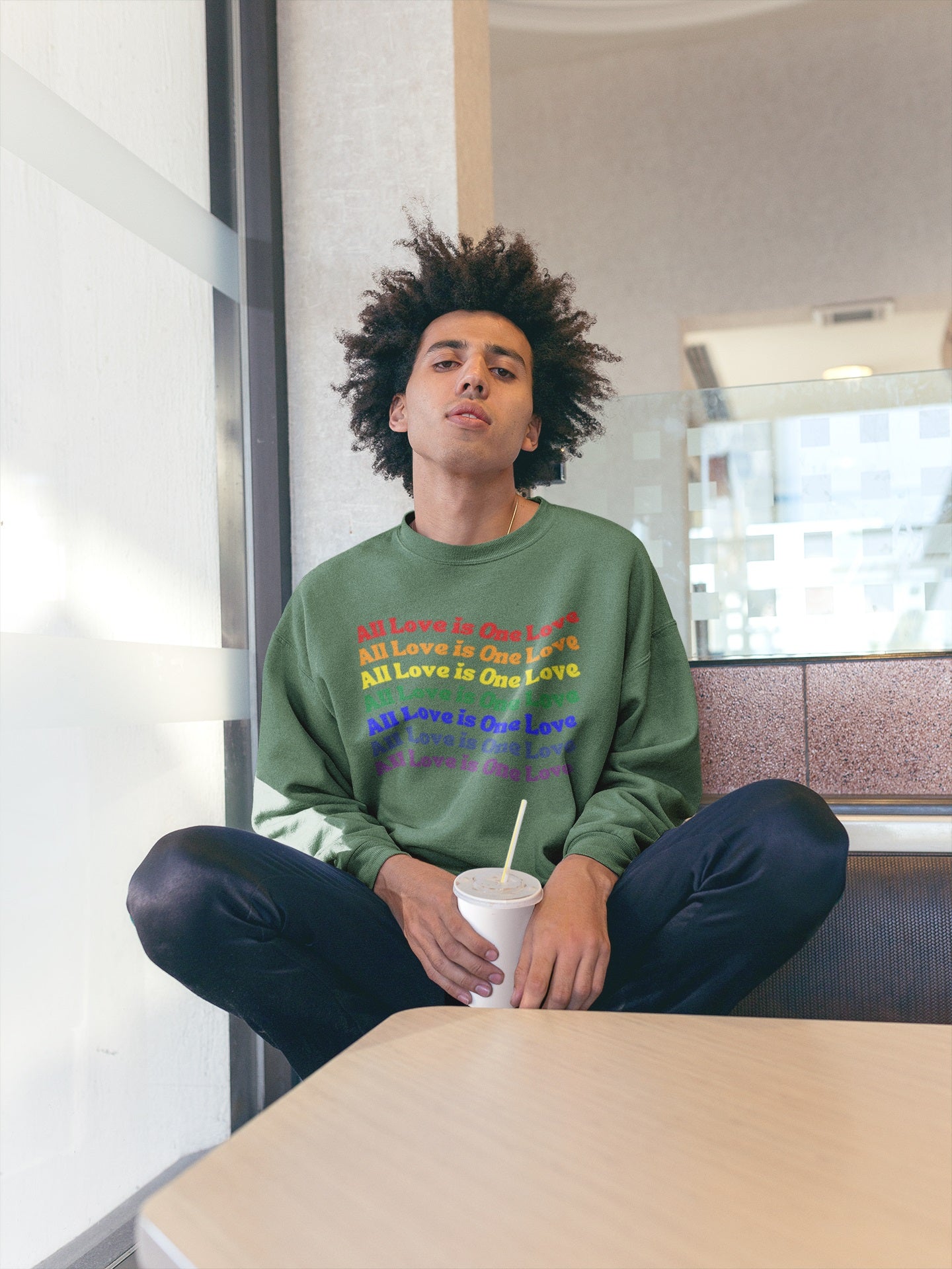 man with afro wearing green nelalane all love sweatshirt sitting in diner