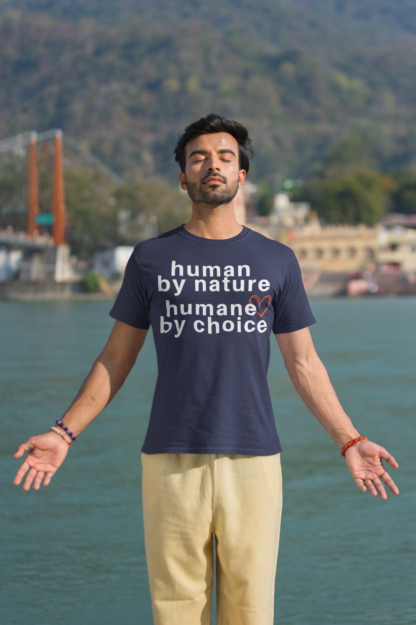 man meditating in the sun wearing a navy blue t-shirt with "human by nature, humane by choice" graphic.