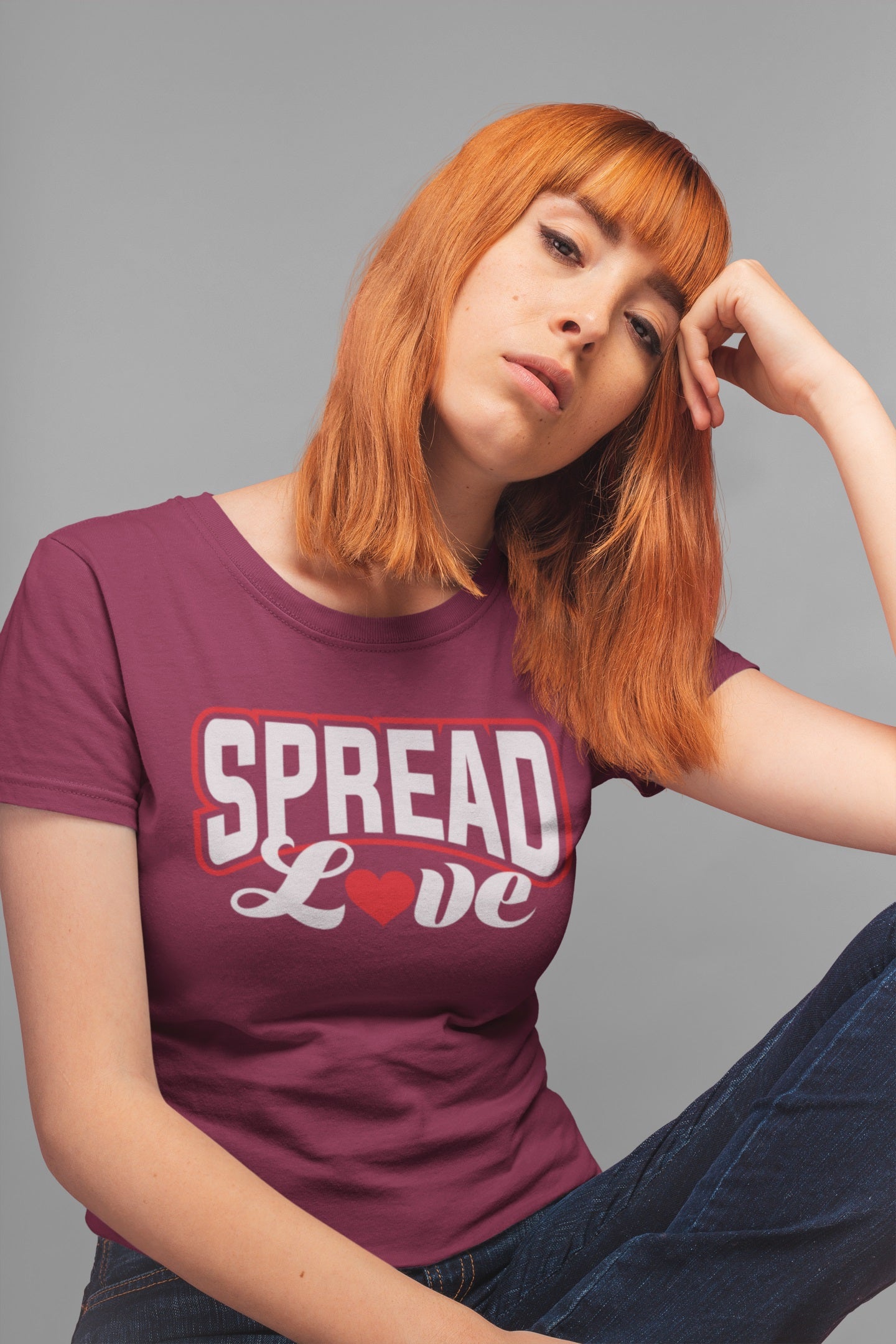 thoughtful red head woman wearing maroon t-shirt with "spread love" graphic with red heart replacing the "o" 