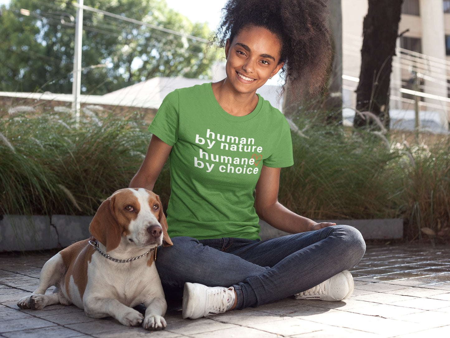 black woman wearing leaf green t-shirt with "human by nature, humane by choice" graphic while petting her  dog