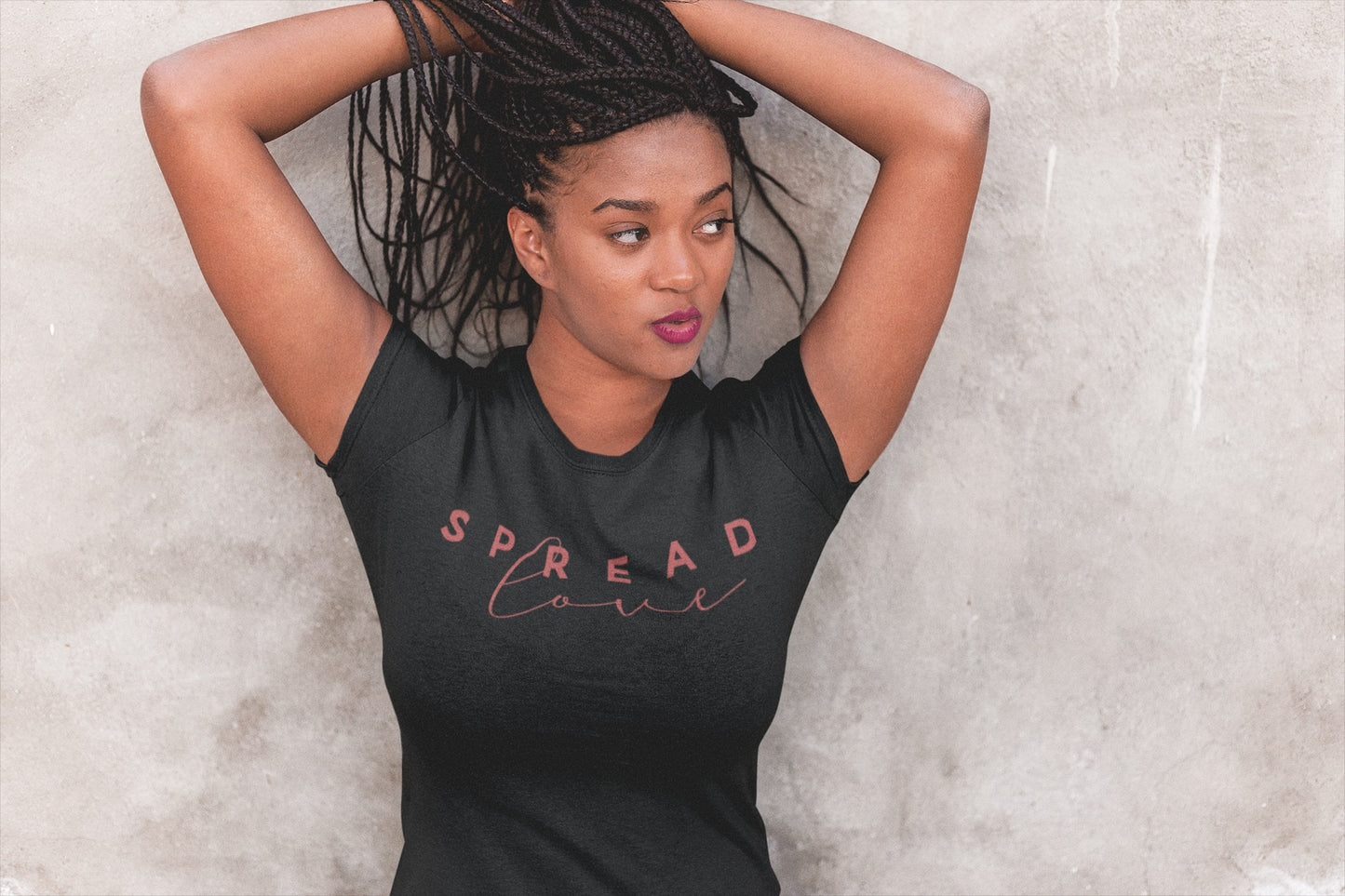 A woman posing with hands raised and elbows out, wearing a gray t-shirt with the text 'SPREAD LOVE' in a decorative font.